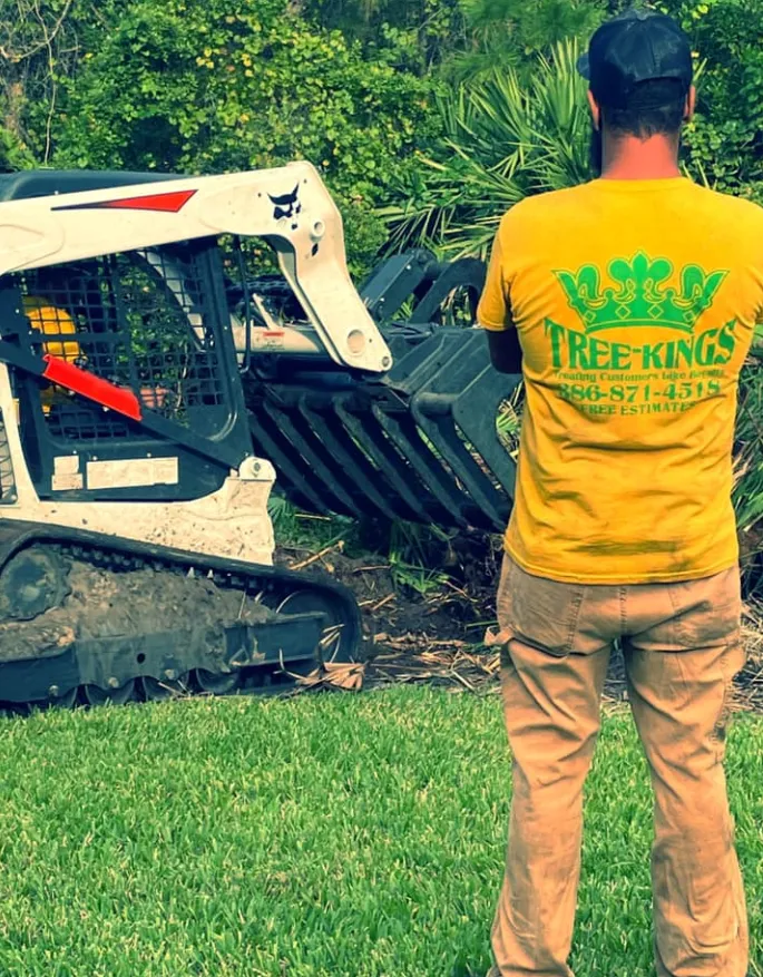 Tree Kings Florida crew member in branded uniform beside a skid-steer loader